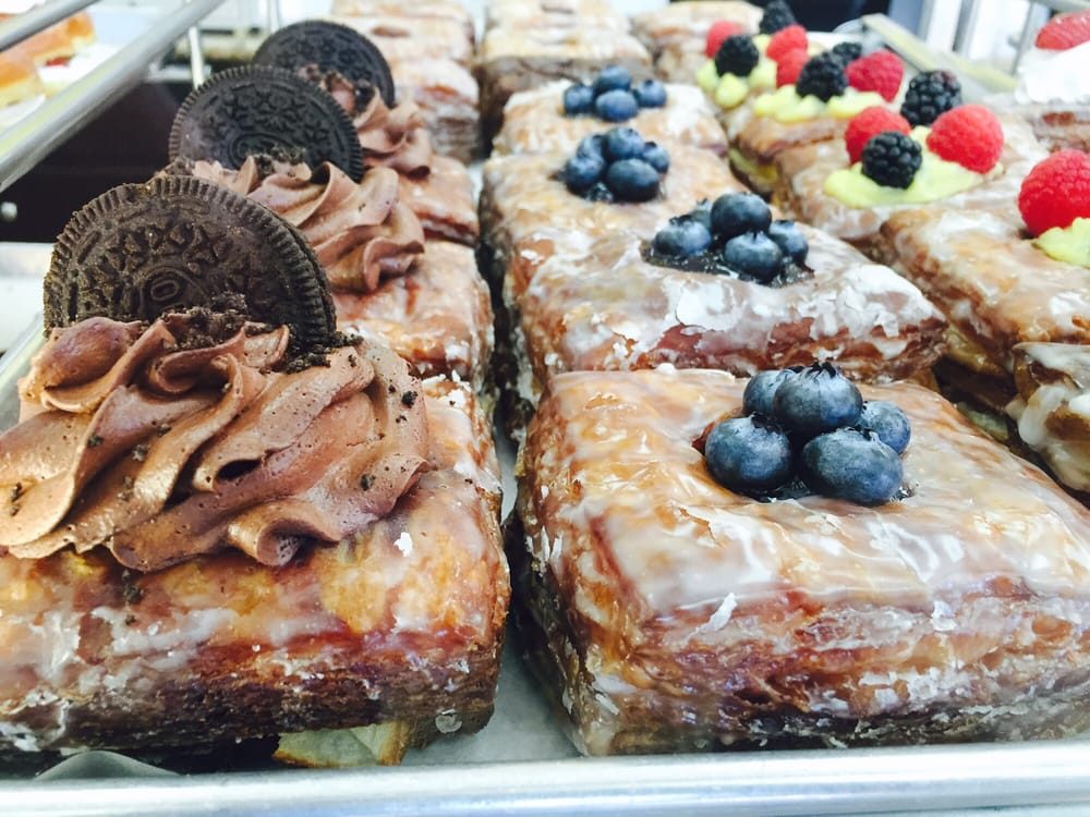 A tray of long glazed pastry bars behind case glass, topped with blueberries, raspberries, blackberries, piped chocolate cream and Oreo cookies.