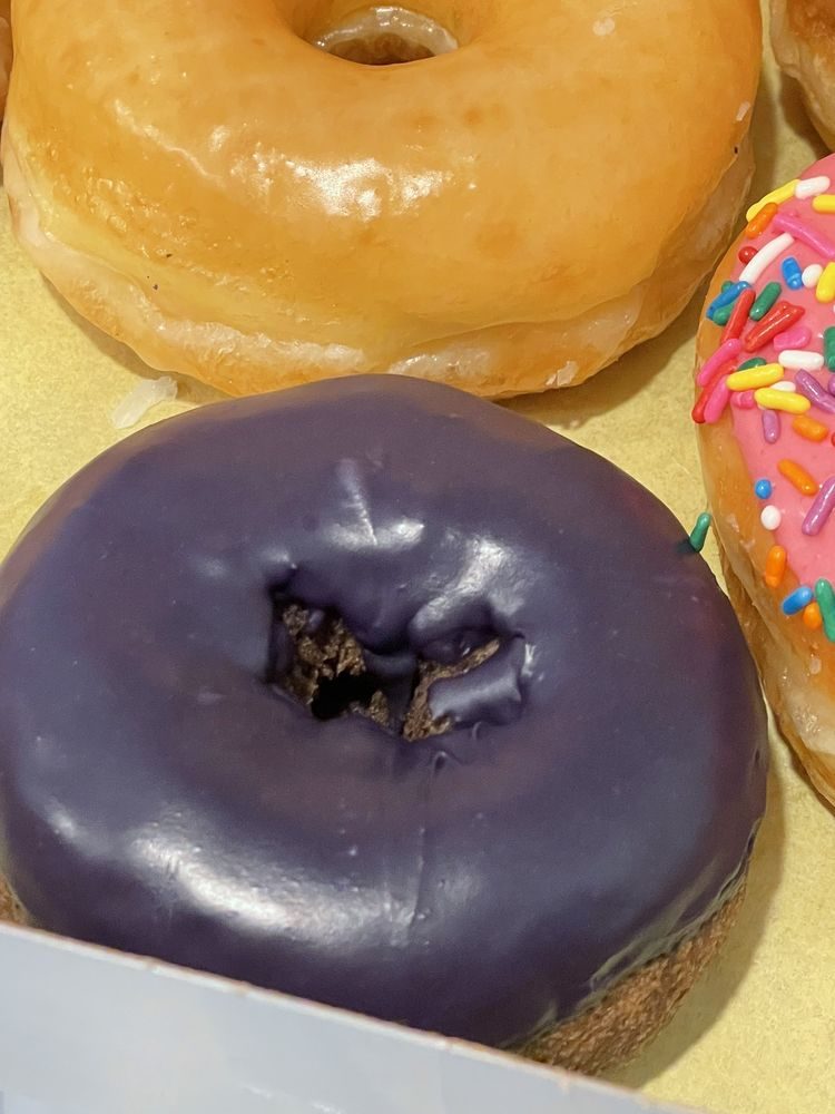 A close view of a plain glazed donut beside a purple ube-frosted cake donut and a pink-iced donut covered in rainbow sprinkles.